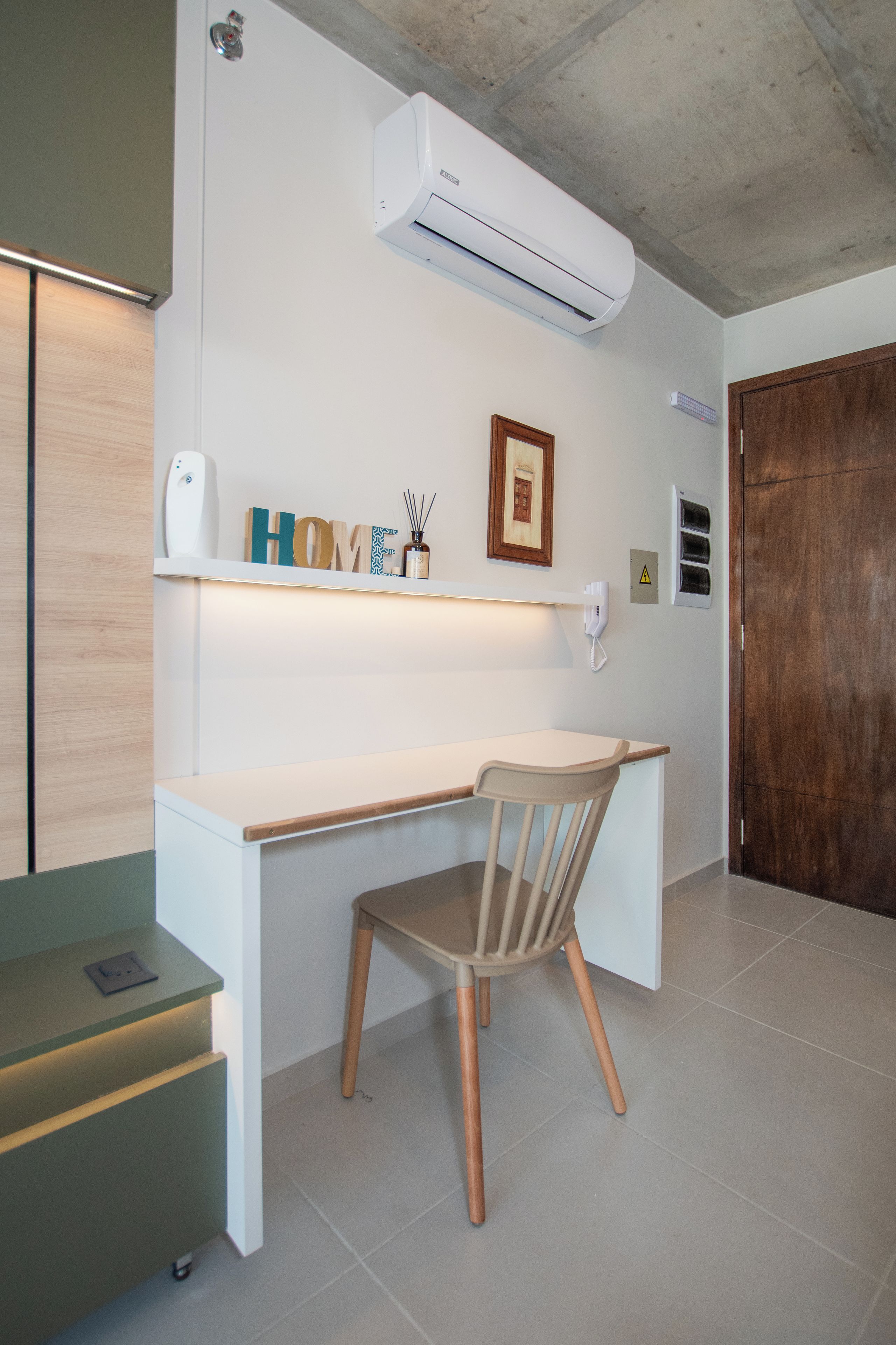 A room with a white desk, a chair, an air conditioning unit, a framed picture, and a wooden door.