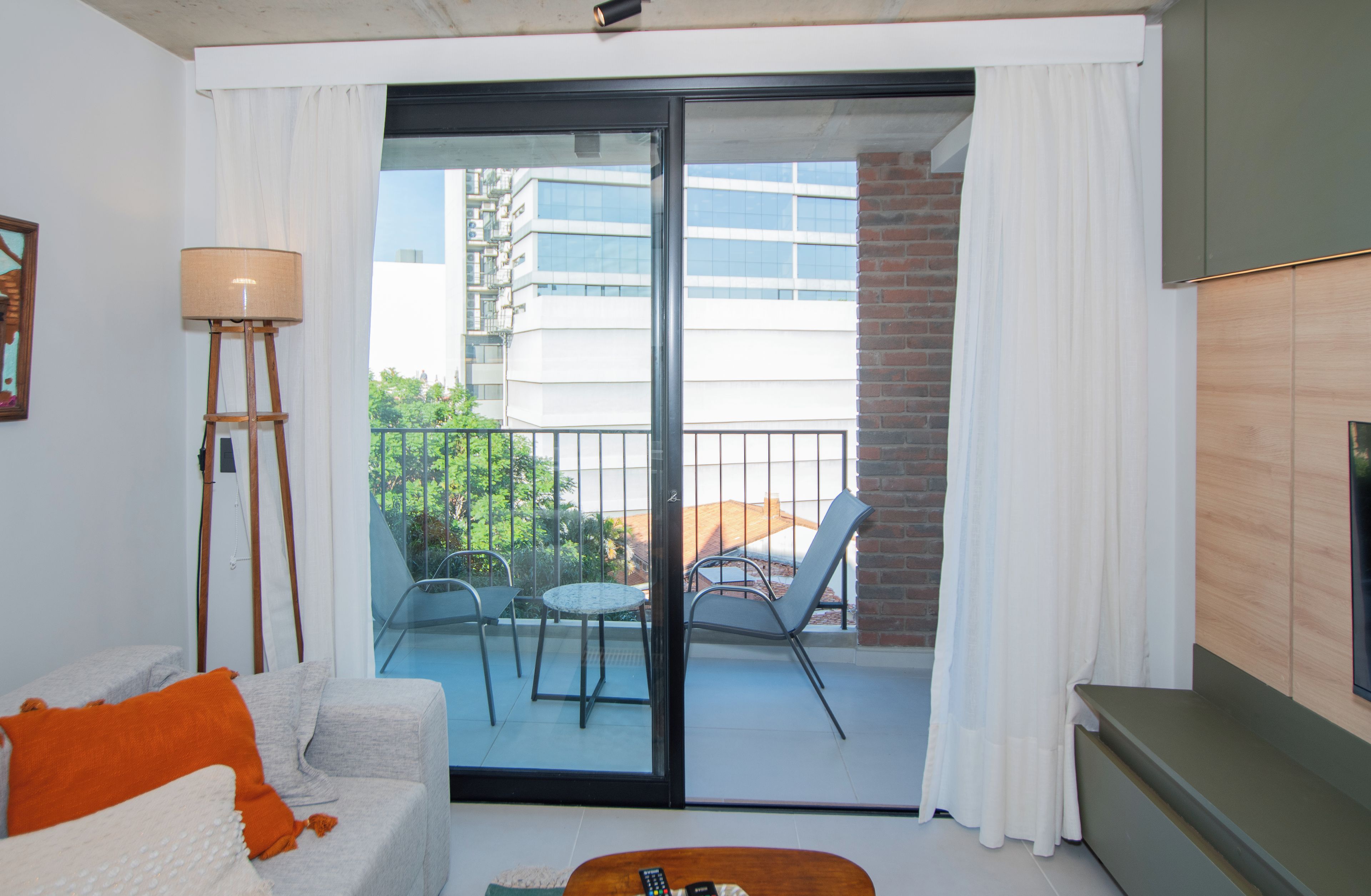 A living room with a sofa, a lamp, a table, and a balcony with chairs and a view of buildings.