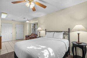 Ein Schlafzimmer mit einem Bett, zwei Nachttischlampen, einem Deckenventilator, einem Fenster mit Jalousien, einer Tür und einem Sessel.