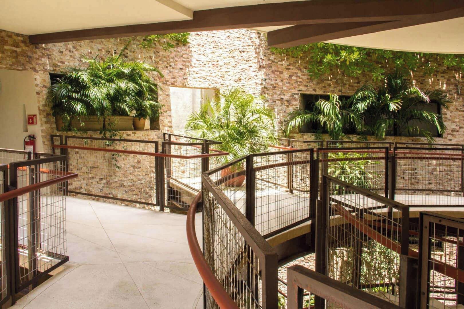 Un atrium de diversos nivells amb pared de maó, barana metàl·lica i plantes en testos.