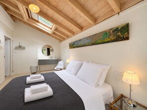 Een slaapkamer met een groot bed, een schilderij aan de muur, een raam en een houten plafond.