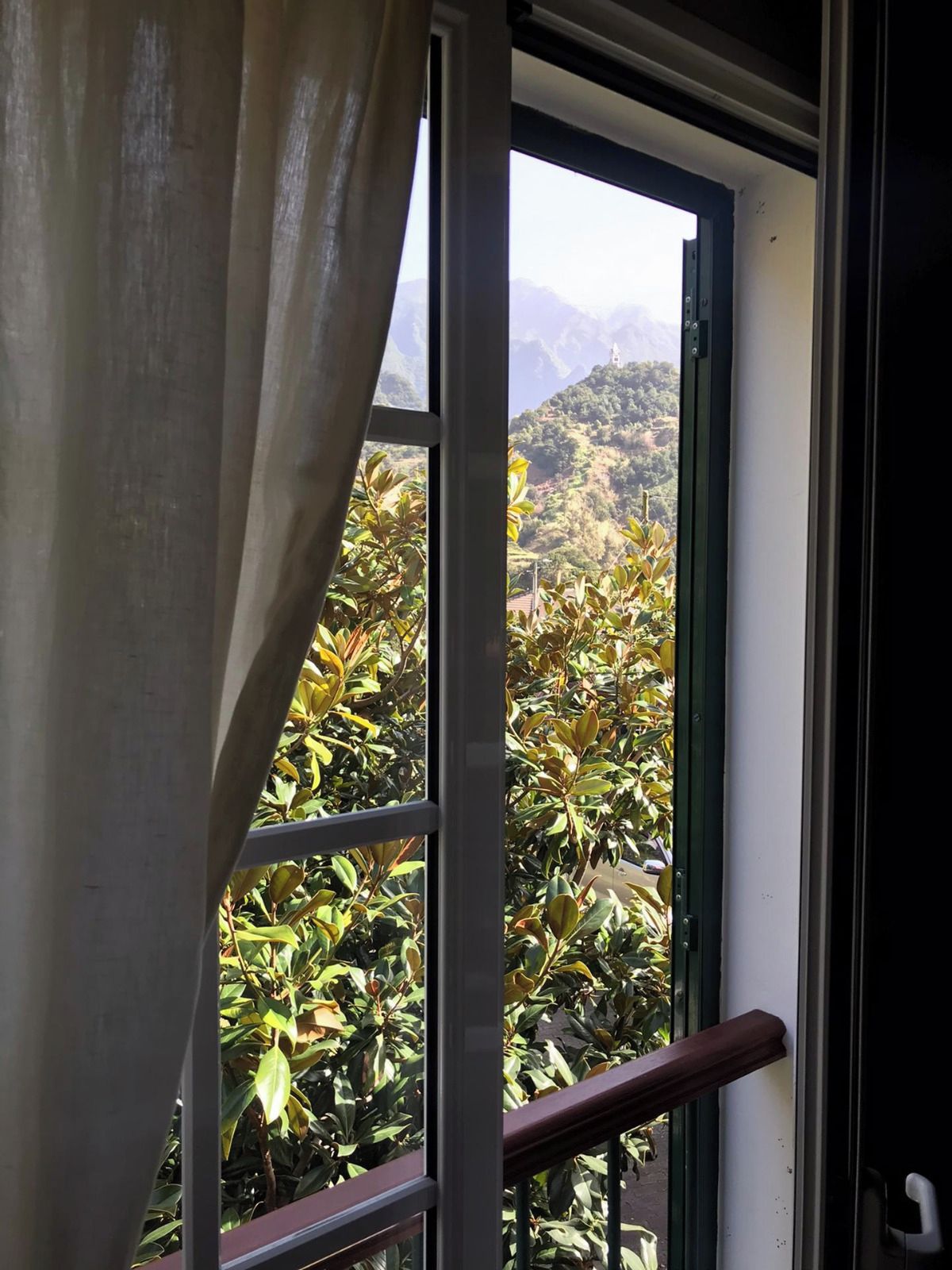 Une fenêtre donnant sur un paysage montagneux et une végétation luxuriante.