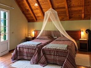 Ein Zimmer mit Holzboden, zwei Betten mit gestreifter Bettwäsche, ein himbeerfarbenes Baldachinbett, Nachttischlampen und ein weißer Teppich.