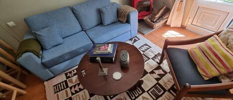Un salon avec un canapé bleu, une table basse ronde agrémentée d’objets décoratifs, un tapis à motifs et un fauteuil avec un coussin à rayures.