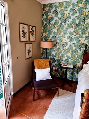 Ein Hotelzimmer mit einem Bett, einem Sessel, einem kleinen Tisch mit Lampe und einer Wand mit Fruchtmuster.