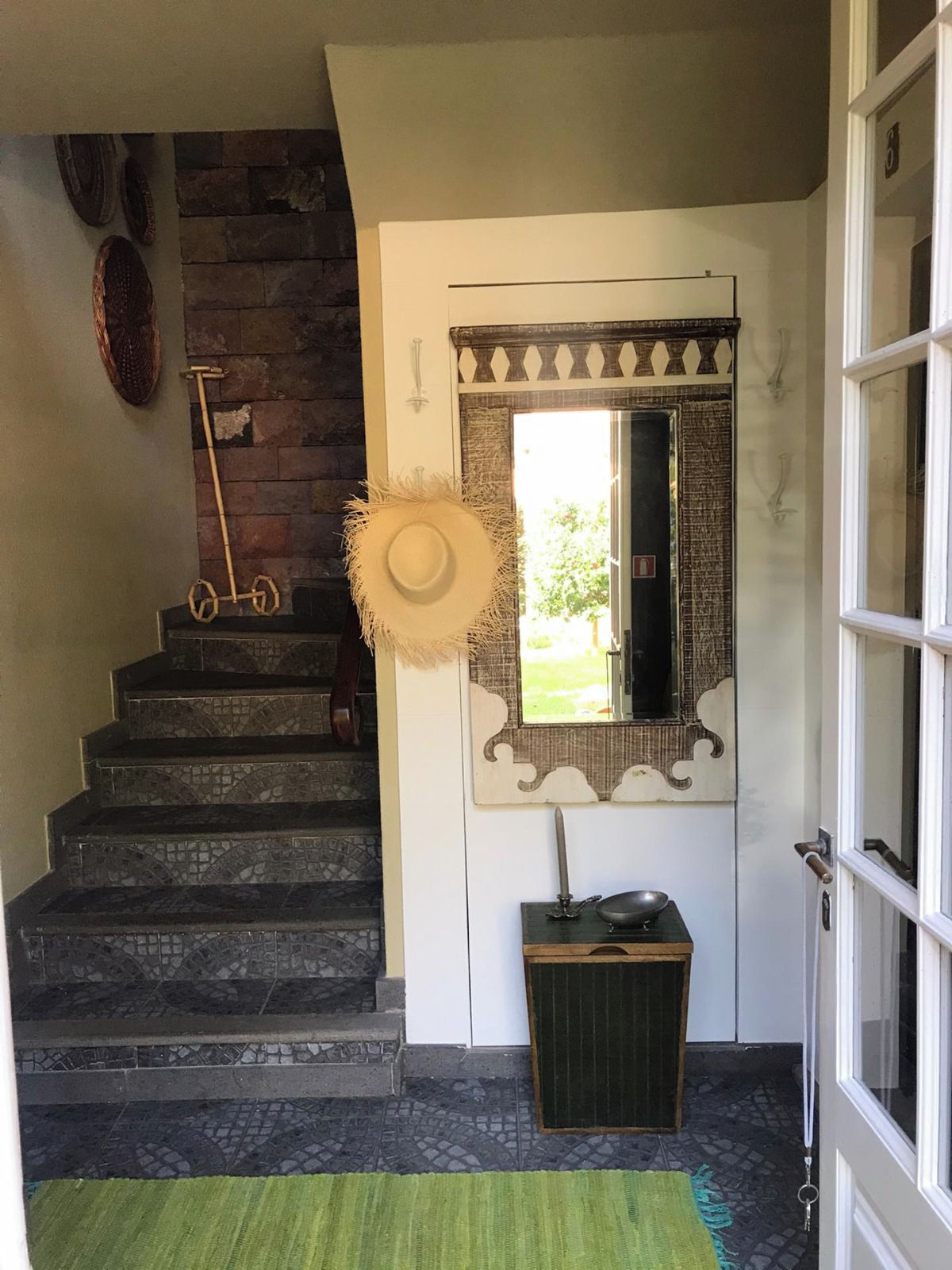 A staircase with a rustic design, a mirror with decorative frame, and a small trash bin.