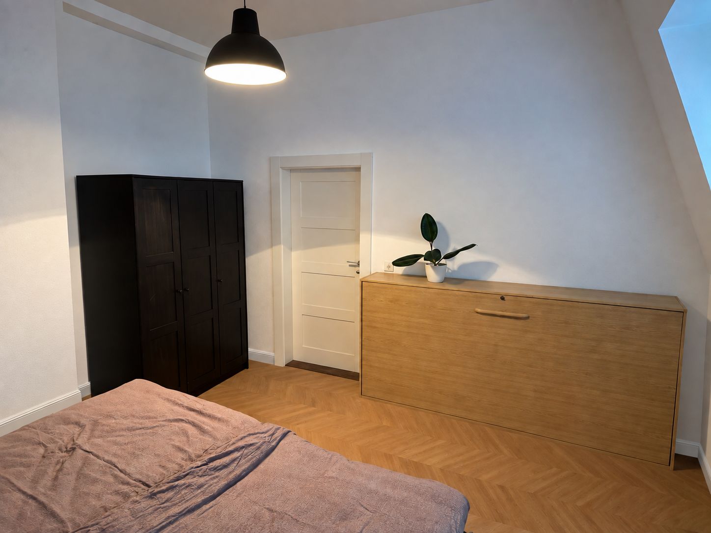 Ein Schlafzimmer mit einem Bett, einem Kleiderschrank, einem Schminktisch und einer Zimmerpflanze.