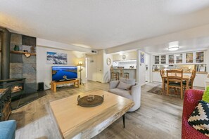 Ein Wohnzimmer mit Kamin, Fernseher, Essbereich mit Stühlen und einer Küche im Hintergrund.
