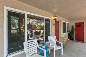 Eine überdachte Terrasse mit roter Tür, weißen Stühlen und einem kleinen Tisch mit einem Blumentopf.