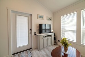 A room with a door, a television on a stand, a cabinet, and a table with a plant. - The Wanderlust Nest Tiny Home with Resort Access (Austin)