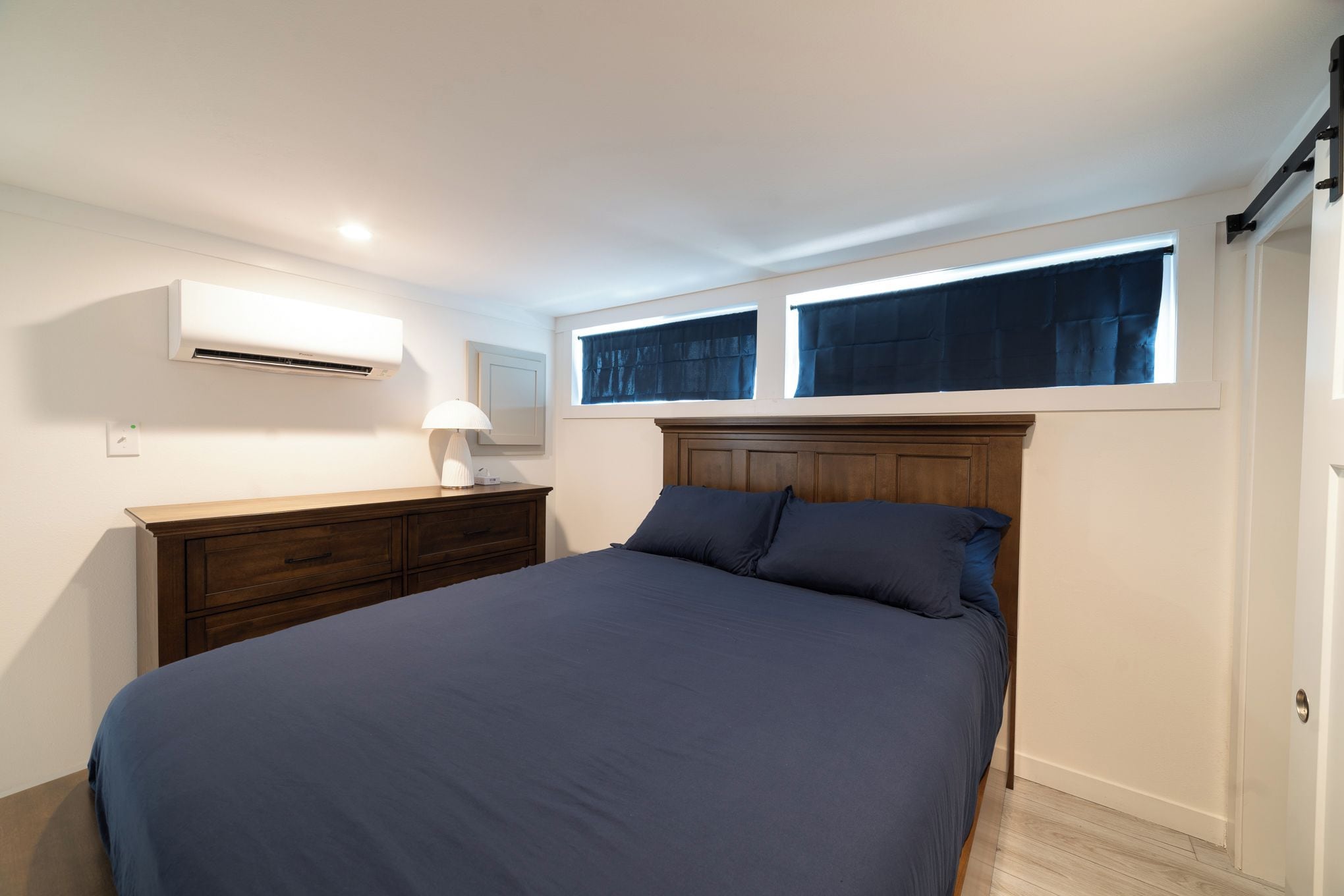 Une chambre à coucher comprenant un lit, une commode, un appareil de climatisation et une fenêtre avec des rideaux.