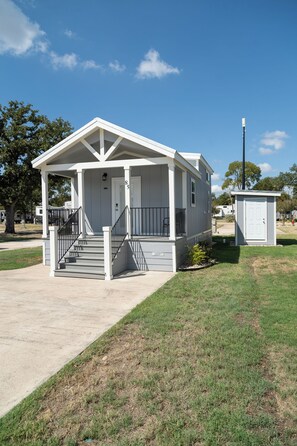 A single-story building with a porch, a staircase leading to the entrance, and a small shed in the background. - The Wanderlust Nest Tiny Home with Resort Access (Austin)
