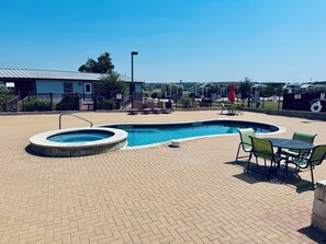 A swimming pool with a hot tub, surrounded by a brick patio, and outdoor seating with a view of residential buildings. - The Wanderlust Nest Tiny Home with Resort Access (Austin)