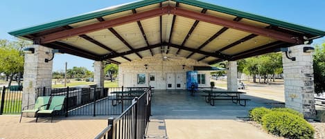 A covered picnic area with stone pillars, picnic tables, and a water dispenser.