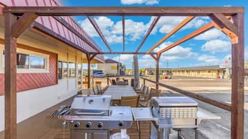 An outdoor patio with a grill, seating, and a view of a motel in the background.