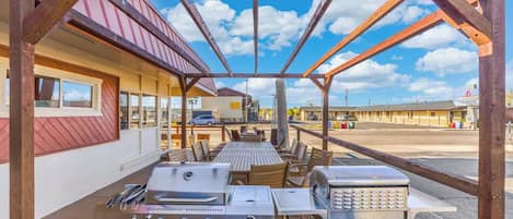 An outdoor patio with a grill, seating, and a view of a motel in the background.
