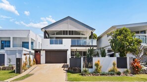 A modern two-story house with a garage, a covered front porch, and a well-maintained garden with various plants.