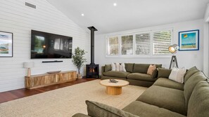 A modern living room with a flat-screen TV, a wood-burning stove, a green sofa, and a round coffee table.