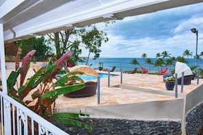 A poolside area with a view of the ocean, lounge chairs, and tropical plants.