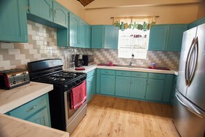 A kitchen with teal cabinets, a black stove, a stainless steel refrigerator, and a window with a curtain.