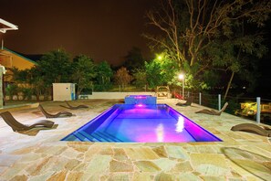 Une piscine dotée d’une terrasse en pierre, entourée de chaises longues et d’arbres.