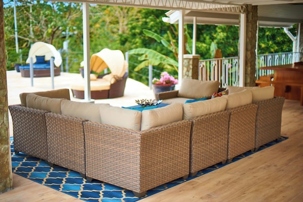 A covered outdoor seating area with a wicker sofa, a dining table, and a chair.