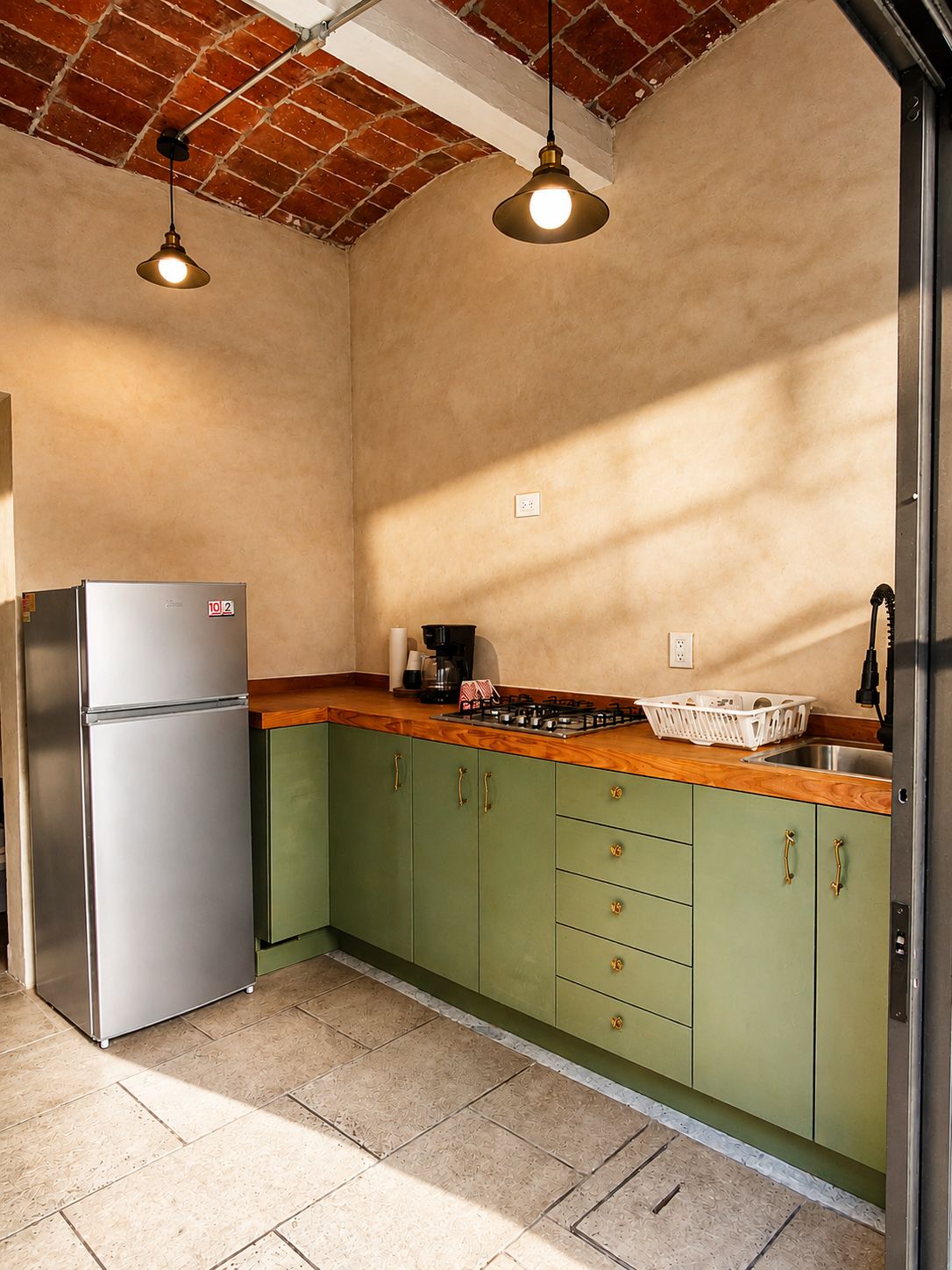 Una cucina con mobili verdi, un frigorifero in acciaio inossidabile, un piano di lavoro in legno e due lampade a sospensione.