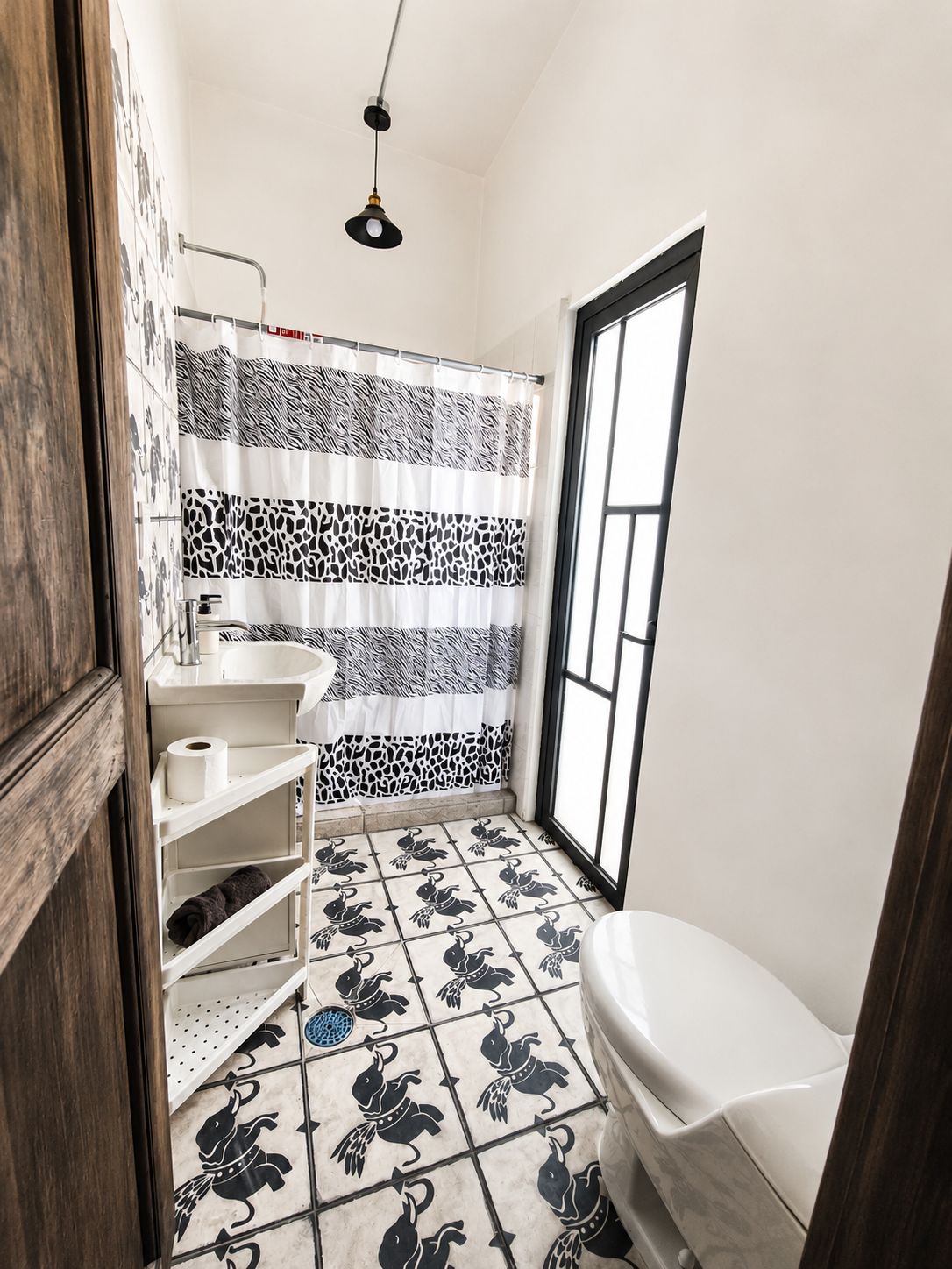 Un baño con inodoro, lavamanos y cortina de ducha con estampado de cebra, además de una ventana.