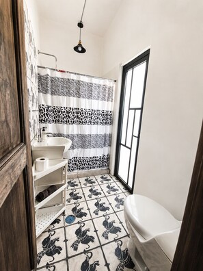 Un baño con inodoro, lavamanos y cortina de ducha con estampado de cebra, además de una ventana.