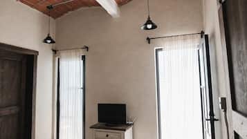 Een kamer met een televisie op een dressoir, een bakstenen plafond en twee ramen met gordijnen.