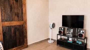 Un soggiorno con porta scorrevole, televisione a schermo piatto, impianto audio, ventilatore e divano.