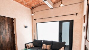 A modern living room with a black sectional sofa, a green throw blanket, and a large window providing natural light. - House in Jalatlaco, pet-friendly and with a garage. (Oaxaca de Juárez)