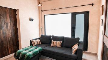 Una sala de estar moderna con un sofá modular negro, una manta verde y un ventanal que proporciona luz natural.