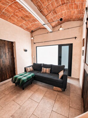 Una sala de estar moderna con un sofá modular negro, una manta verde y un ventanal que proporciona luz natural.