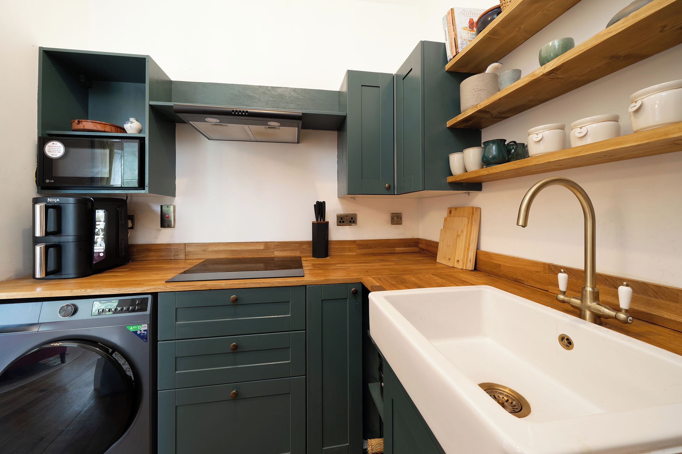 A compact kitchen with a built-in washing machine, a coffee maker, and a sink with a vintage faucet.