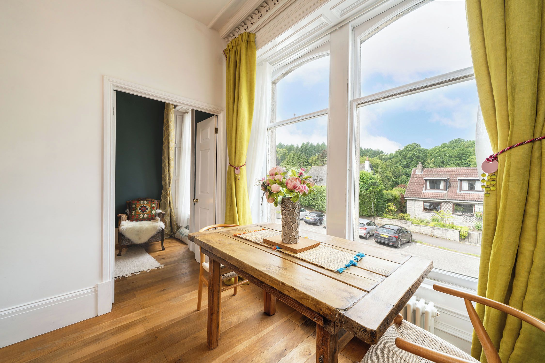 A dining area with a wooden table, chairs, and a view of the outside through large windows.