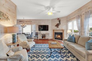 A cozy living room with a fireplace, a ceiling fan, and a television. - Beachfront Villa on Tybee Island - Sleeps 8, Steps to the Sand (Tybee Island)