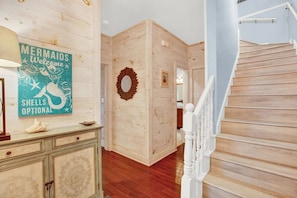 A wooden interior with a staircase, a decorative wall with a mermaid sign, and a round mirror. - Beachfront Villa on Tybee Island - Sleeps 8, Steps to the Sand (Tybee Island)