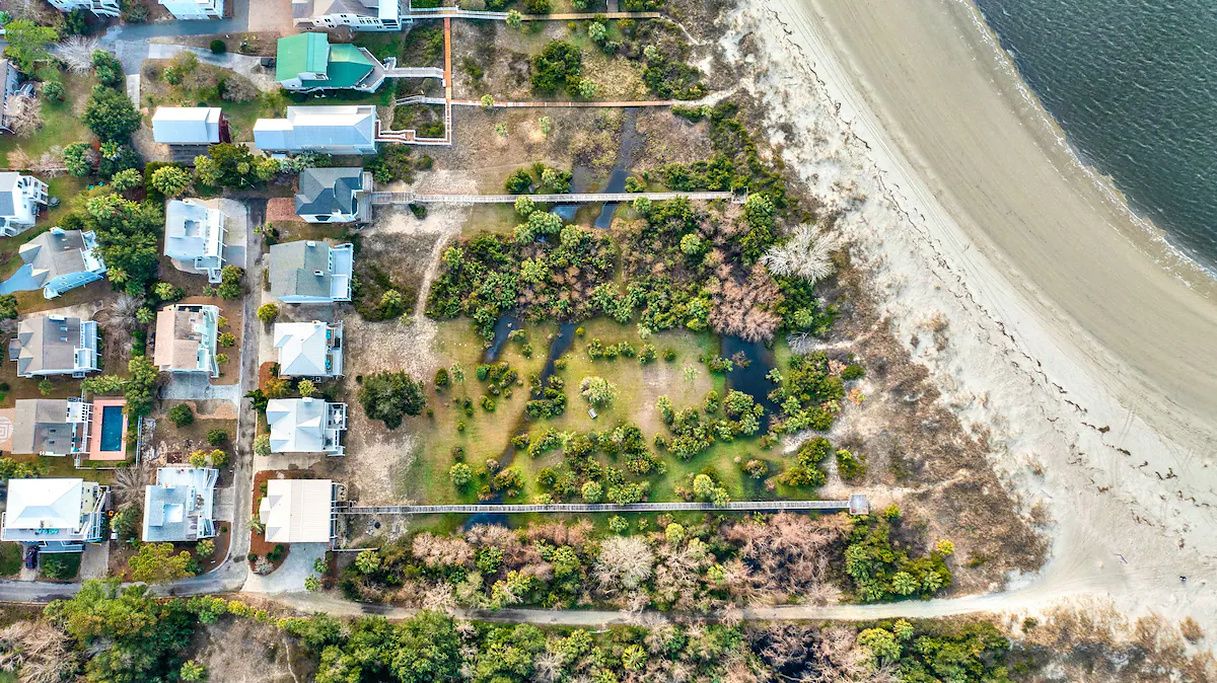 An aerial view of a coastal residential area with houses, a beach, and a waterway.