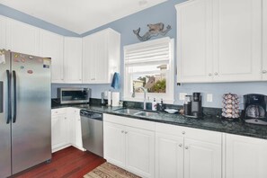 A kitchen with white cabinets, stainless steel appliances, a granite countertop, and a window with blinds. - Beachfront Villa on Tybee Island - Sleeps 8, Steps to the Sand (Tybee Island)
