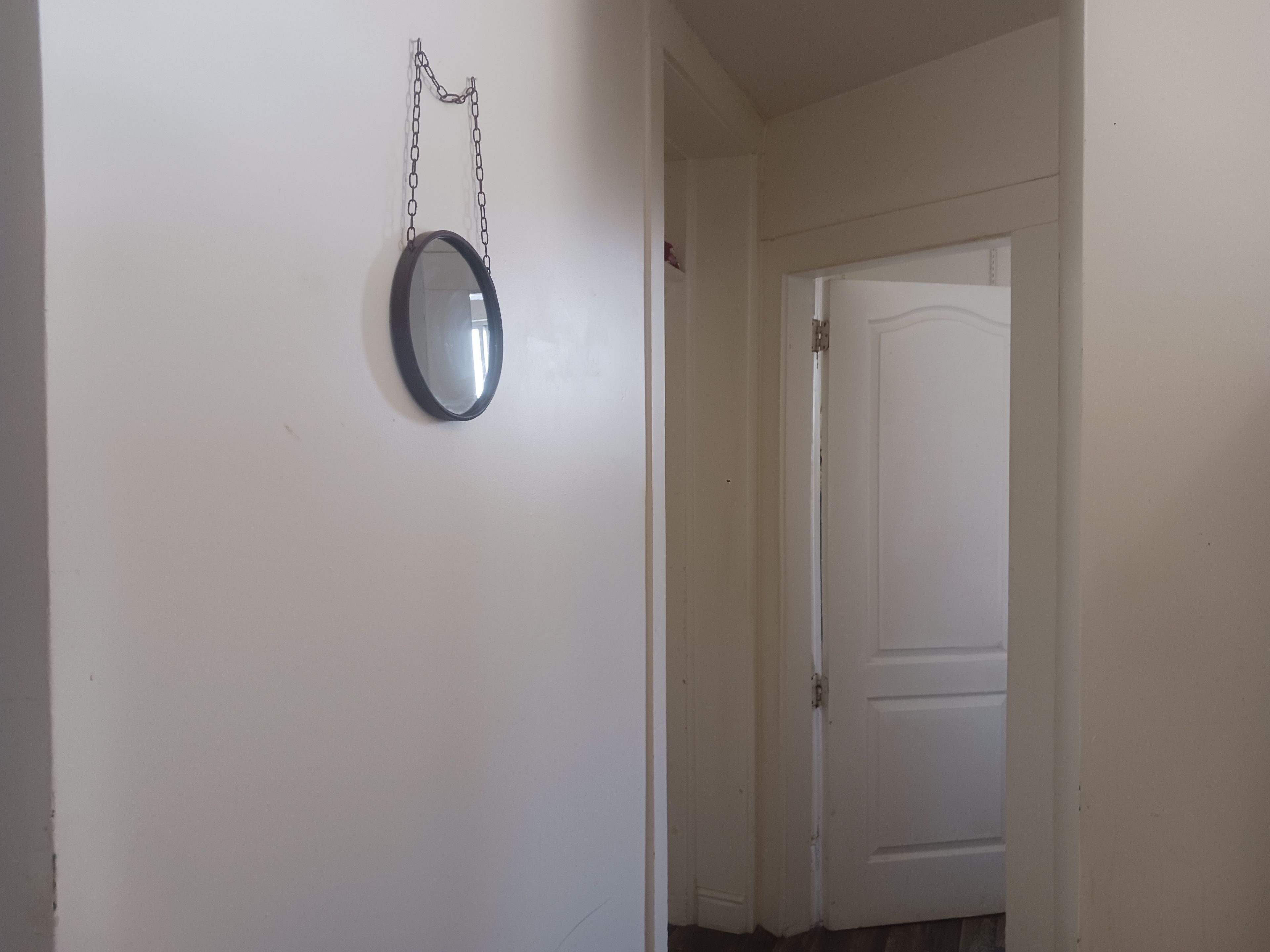 A hallway with a white door and a round mirror hanging on the wall.