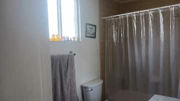 A bathroom with a toilet, a shower curtain, a window with a view of ducks, and a towel hanging on the wall.