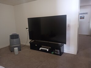 Habitación con un televisor de pantalla grande sobre un mueble, un altavoz pequeño y un enchufe en la pared.