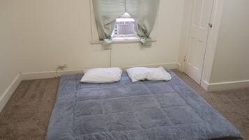 A room with a single bed, a window with curtains, a door, and a carpeted floor.