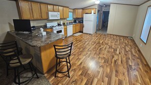 A kitchen with wooden cabinets, a microwave, a stove, a refrigerator, and a bar area with stools. - Wonderful 3-bedroom mobile home with AC in Hyannis (Hyannis)