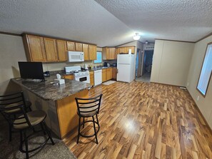 Una cocina con armarios de madera, microondas, estufa, refrigerador y una barra con taburetes.