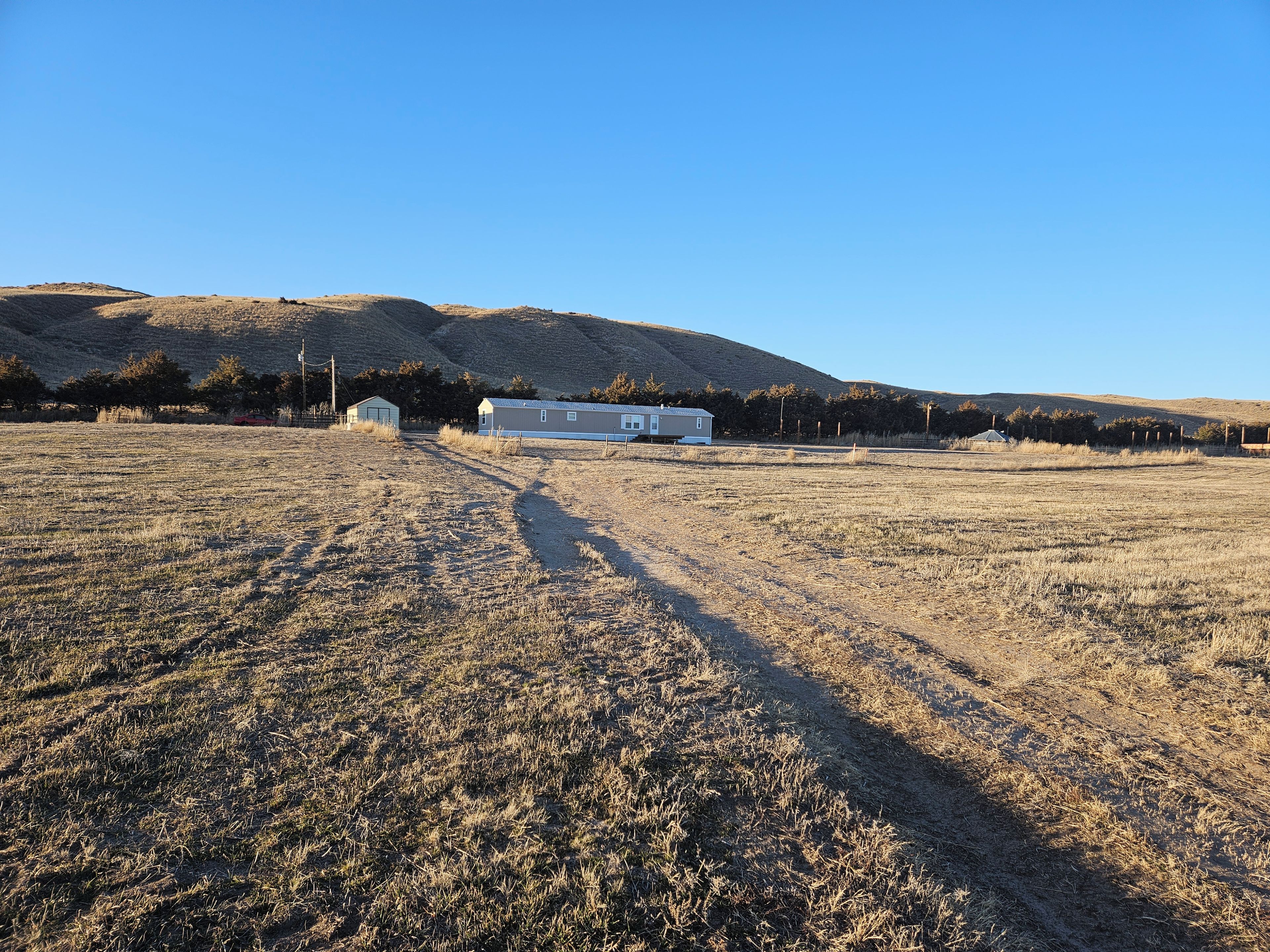 Ländliche Landschaft mit einem einzelnen Haus, blauem Himmel und hügeliger Kulisse.