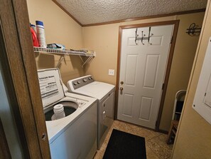 A laundry room with a washer and dryer, a shelf with cleaning supplies, and a door with a coat rack.