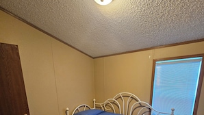 A bedroom with a single bed, a door, a window with blinds, and a carpeted floor. - Wonderful 3-bedroom mobile home with AC in Hyannis (Hyannis)