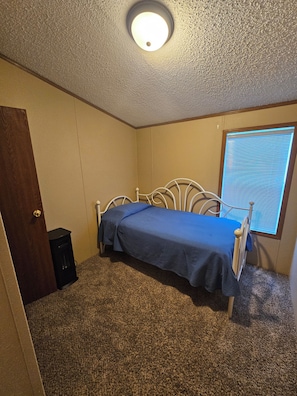 Un dormitorio con una cama individual, una puerta, un ventanal con persianas y suelo alfombrado.